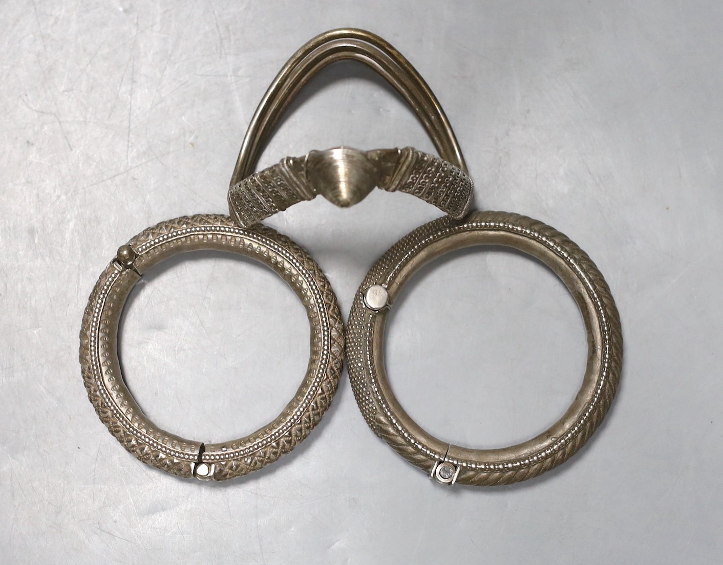 Two 20th century Indian white metal hinged bracelets and a similar shaped bangle.